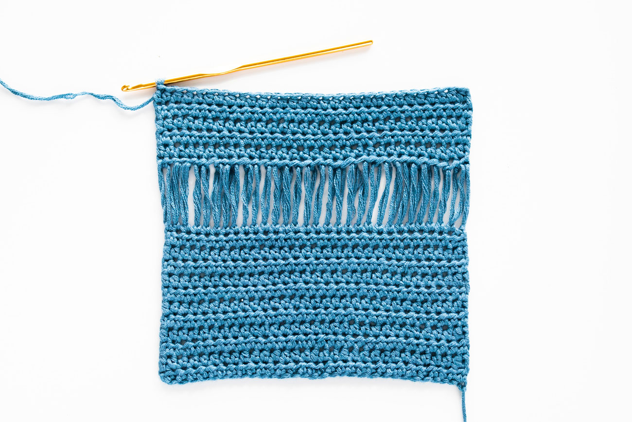 swatch of drop loop crochet stitch in cotton bamboo yarn with gold crochet hook