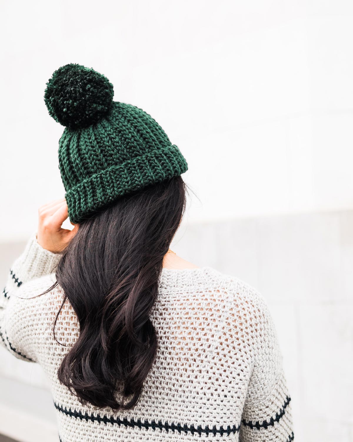 back view of woman wearing chunky crochet beanie with large pom pom made in green wool-acrylic yarn